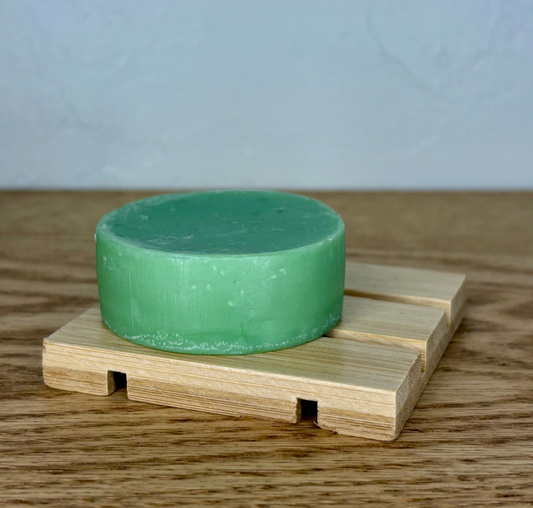 Green soap bar on a wooden soap dish with a plain background
