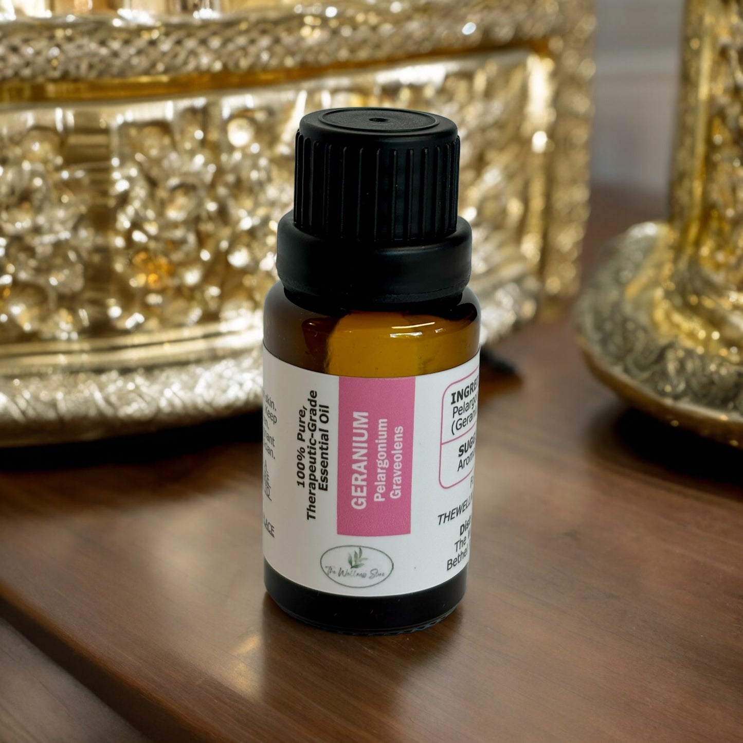 Geranium Essential oil on a wood surface wit gold bowls in the background