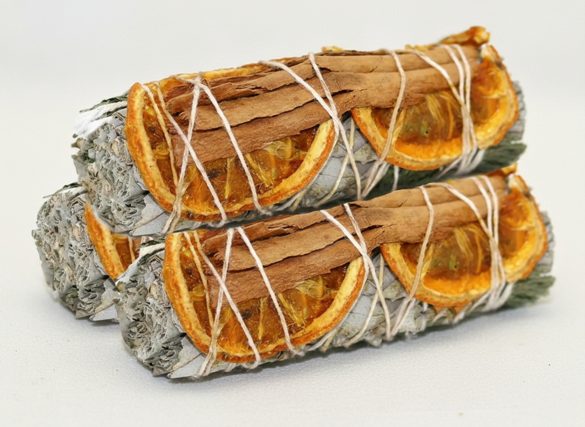 Two bundles of sage and cinnamon sticks with orange slices tied together on a white background