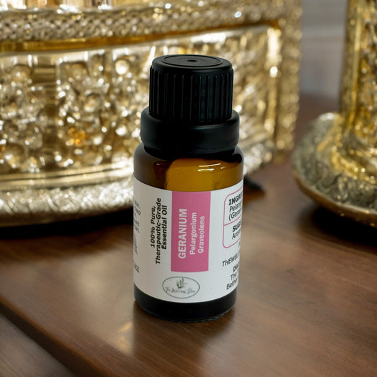 Geranium Essential oil on a wood surface wit gold bowls in the background
