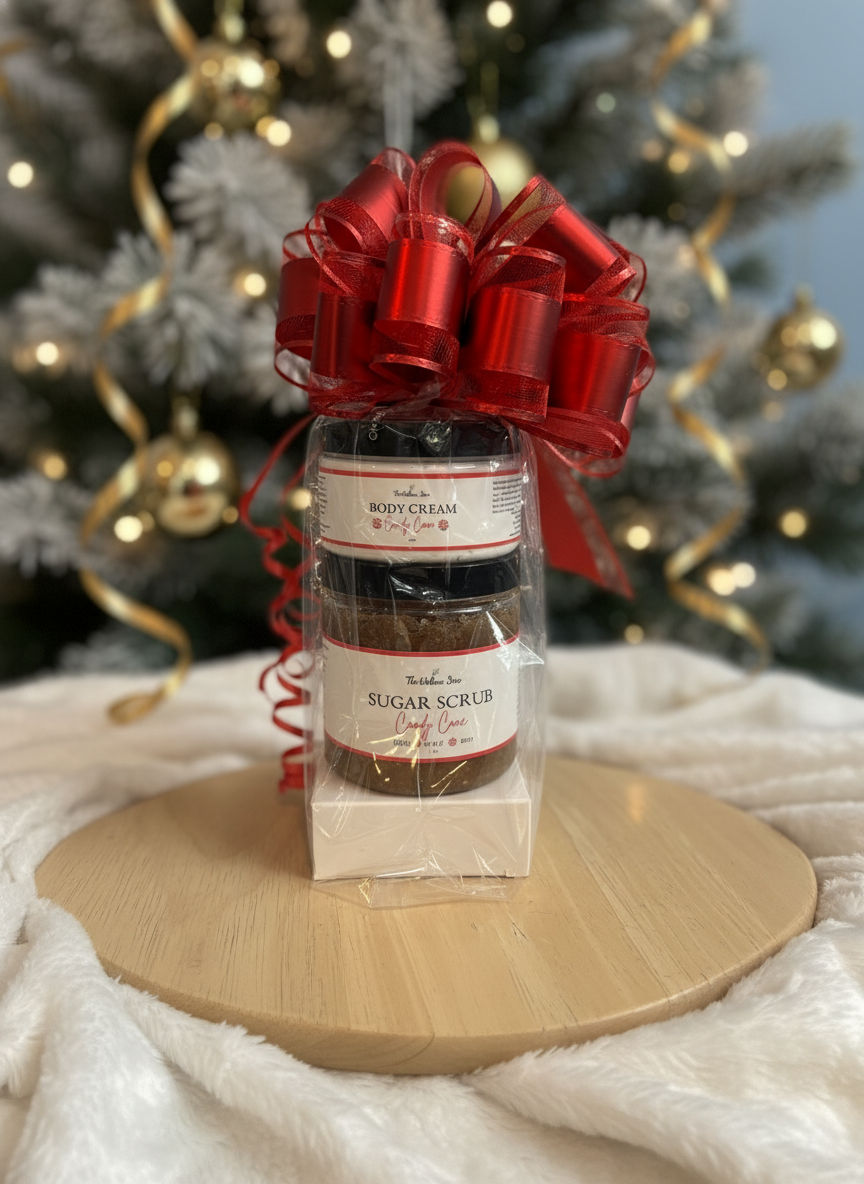 Gift set with Candy Cane body cream, soap and sugar scrub under a red bow on a wooden stand with a Christmas tree in the background.